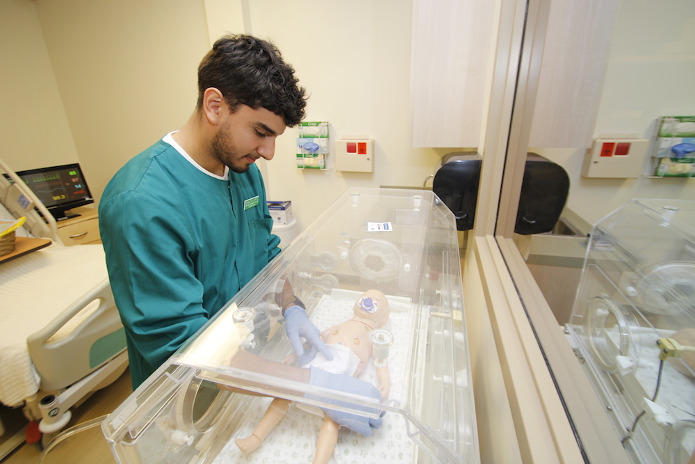 A healthcare student adjusts the oxygen mask on an infant simulator